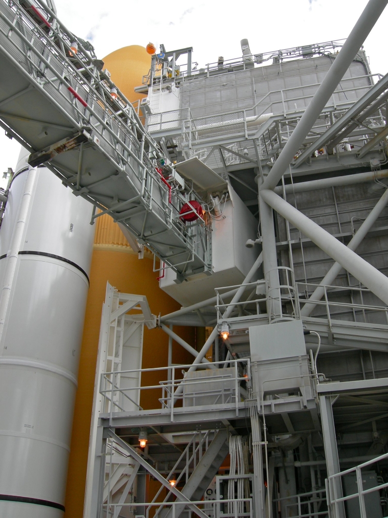 Large-format photograph: Orbiter Access Arm in extended position with RSS mated to the Orbiter at Pad A, viewed from below, looking across and up from the FSS. Photo by Andrew P. Scheer, former Pad Flow Manager at Complex 39, Kennedy Space Center, Florida.